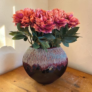 Koraalroze zonsondergangoranje magenta pioenrozenstelen in een vaas van studio-keramiek.