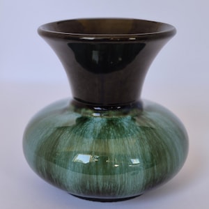 May include: A ceramic vase with a bulbous body and a flared rim. The lower portion features a glossy glaze with blended shades of deep forest green and lighter mint green, while the neck and rim are finished in a solid, dark espresso brown.