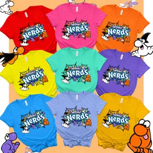 May include: A collection of nine short-sleeve t-shirts in various colors including red, pink, orange, yellow, teal, purple, blue, light purple, and gold. Each shirt features a graphic of a spider web with the text Spooky NERDs and ghosts.