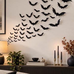 May include: A collection of black bat-shaped wall decals arranged in a swarm pattern on a light-coloured wall. The bats vary in size and are positioned to create a dynamic, flying effect across the surface, ranging from large to small silhouettes.