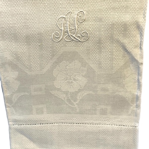 May include: White linen hand towel with a floral pattern and embroidered monogram "A.L."