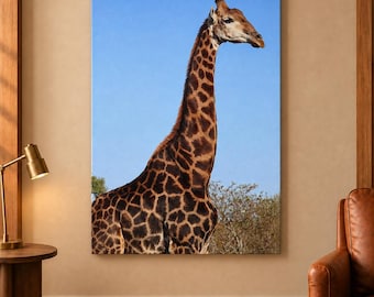 May include: A rectangular wall art print featuring a giraffe with a distinct brown and tan reticulated coat pattern. The giraffe is positioned against a clear blue sky, with the tops of green trees visible at the bottom of the frame.