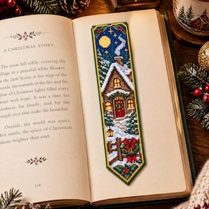 May include: A rectangular cross-stitch bookmark featuring a winter scene with a snow-covered house, a chimney with smoke, a yellow moon, and a red door with a wreath. The design includes pine trees, a wooden fence, and a red bow, all bordered in green.