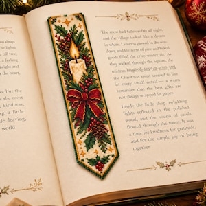 May include: A rectangular cross-stitch bookmark featuring a lit candle, a red bow, pine branches, and red berries on a cream background. The bookmark has a pointed bottom edge and is placed on an open book page with printed text about winter.