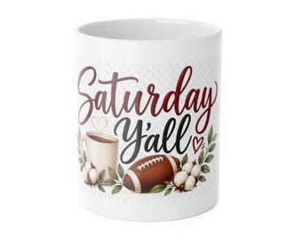 Könnte beinhalten: Ein weißer Keramikbecher mit dem Schriftzug "Saturday Y'all" in roten und schwarzen Schriftarten. Das Design zeigt einen braunen Football, eine Kaffeetasse mit herzförmigem Dampf sowie weiße Baumwollblüten mit grünen Blättern.