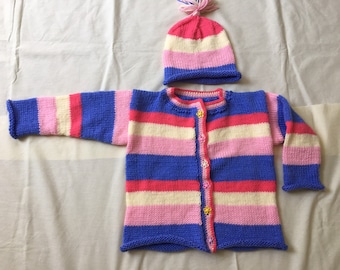 May include: A striped knitted baby sweater and hat set in pink, white, and blue colors. The sweater has a button closure and the hat has a pom-pom on top.