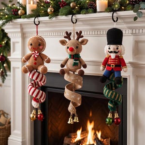 Pode incluir: Três enfeites de Natal de crochê pendurados em ganchos pretos. À esquerda, um boneco de gengibre marrom com uma cauda listrada de vermelho e branco. No centro, uma rena bege com cauda de juta. À direita, um quebra-nozes com cauda verde.