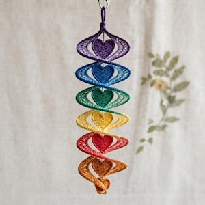 Può includere: Una decorazione verticale da appendere con sei cuori all'uncinetto in una sequenza di colori arcobaleno: viola, blu, verde, giallo, rosso e arancione. Ogni cuore è racchiuso in una cornice ovale all'uncinetto abbinata, uniti a spirale.