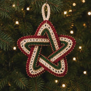May include: A five-pointed star ornament crafted from crocheted yarn in deep red, forest green, and cream colors. The star features an intricate woven design accented with small gold beads along the edges and a matching cream hanging loop.