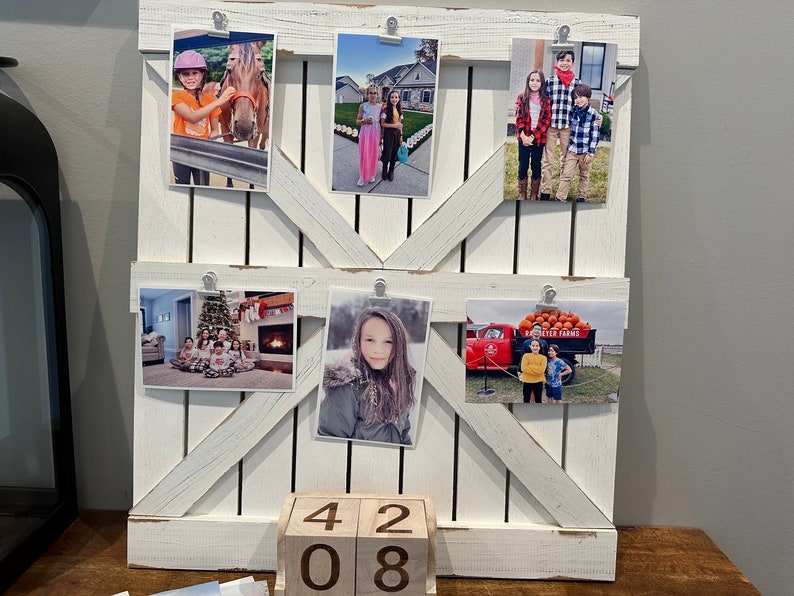 May include: White wooden photo display with five pictures of children. The pictures are held in place with clips. The display is on a table with a wooden block calendar that reads "42 08".