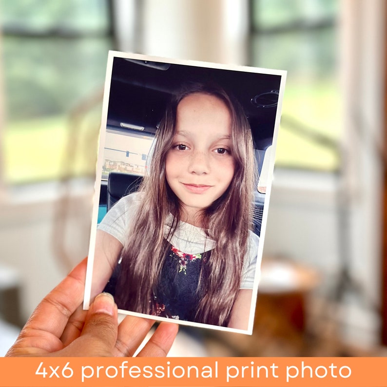 May include: A 4x6 inch professional print photo of a young girl with long brown hair, wearing a white shirt and a floral print overall dress. She is smiling and looking at the camera.