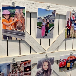 May include: A white wooden picture frame with a rustic design, holding multiple photos of children. The photos are held in place with white clips. The photos show children in various settings, including a horse, a pumpkin patch, a Christmas tree, and a red truck.