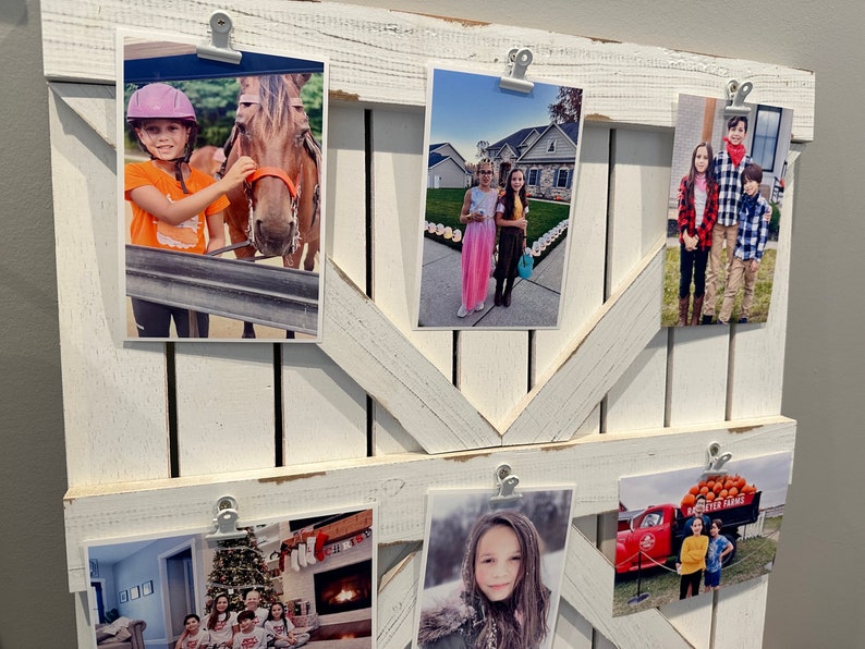 May include: A white wooden picture frame with a rustic design, holding multiple photos of children. The photos are held in place with white clips. The photos show children in various settings, including a horse, a pumpkin patch, a Christmas tree, and a red truck.
