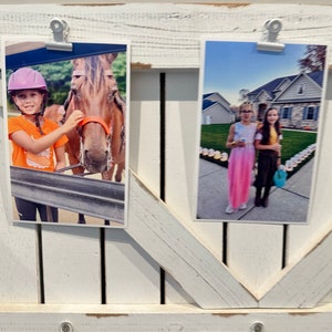 May include: Two photos displayed on a white wooden frame. The photo on the left shows a young person wearing a purple helmet and an orange shirt, petting a brown horse. The photo on the right shows two young people standing in front of a house with lights on the ground. The person on the left is wearing a pink dress and the person on the right is wearing a brown dress.
