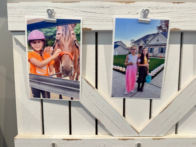 May include: Two photos displayed on a white wooden frame. The photo on the left shows a young person wearing a purple helmet and an orange shirt, petting a brown horse. The photo on the right shows two young people standing in front of a house with lights on the ground. The person on the left is wearing a pink dress and the person on the right is wearing a brown dress.