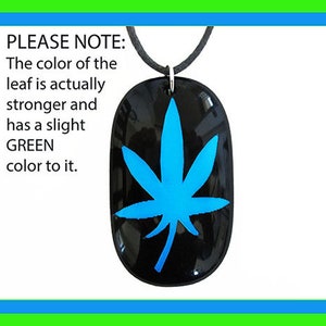May include: Black oval pendant with a bright blue cannabis leaf design. The pendant hangs from a black cord. The text in the image says the leaf color is stronger and has a slight green color to it.