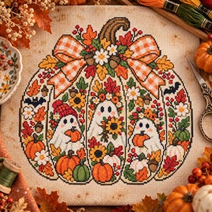 Puede incluir: Un bordado de punto de cruz sobre tela beige con el contorno de una gran calabaza relleno de motivos otoñales, incluyendo tres fantasmas blancos, girasoles, calabazas naranjas, bellotas y un lazo a cuadros en la parte superior.