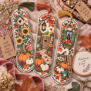 Peut inclure: Trois marque-pages rectangulaires au point de croix sur le thème de l'automne, ornés de tournesols, de citrouilles, de nichoirs et de lanternes. Chaque marque-page est terminé par un pompon coloré et présente des motifs brodés aux tons saisonniers.