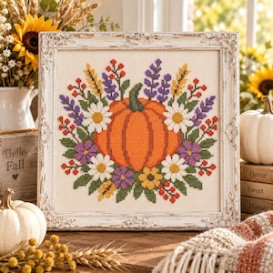 Peut inclure: Une broderie au point de croix carrée représentant une citrouille orange centrale entourée d'une couronne colorée de marguerites blanches, de fleurs violettes, de fleurs jaunes, de feuilles vertes et de baies rouges, dans un cadre orné blanc vieilli.