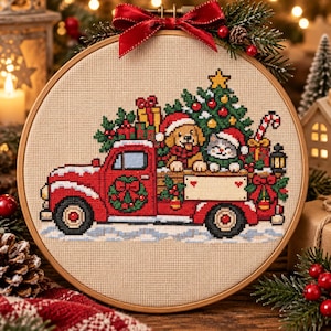 May include: A circular embroidery hoop containing a cross-stitch pattern of a red pickup truck carrying a Christmas tree, a dog, and a cat wearing Santa hats. The truck features a wreath on the door and a blank sign on the side, topped with a red bow.