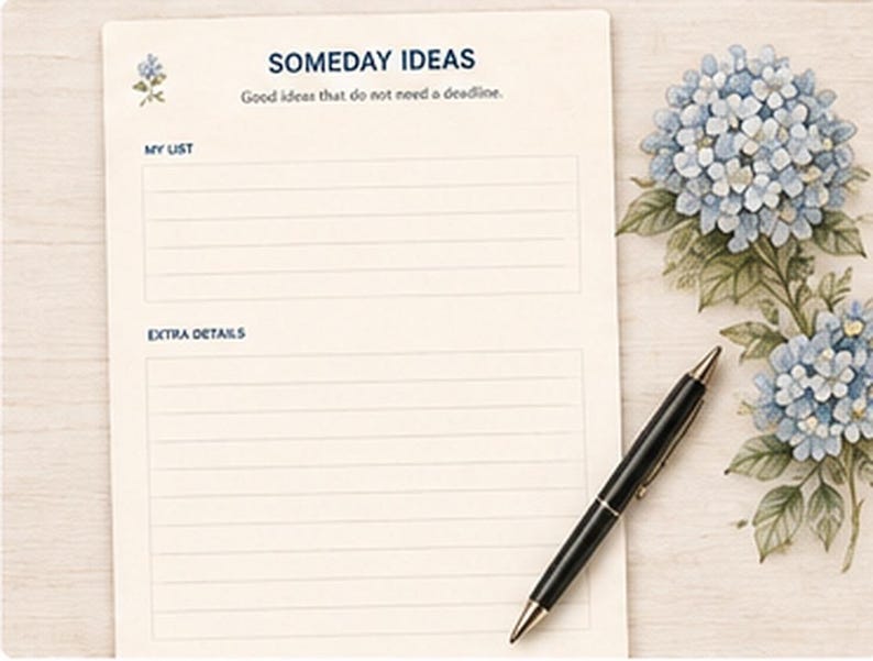 May include: A cream-colored notepad with blue text reading SOMEDAY IDEAS, Good ideas that do not need a deadline, MY LIST, and EXTRA DETAILS. The page features blue hydrangea illustrations and is accompanied by a black ballpoint pen.