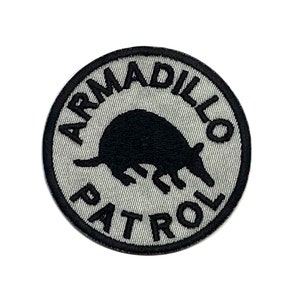 May include: A gray and black embroidered patch with the text "Armadillo Patrol" and a black silhouette of an armadillo.