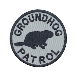 May include: A gray and black embroidered patch with a groundhog silhouette and the text "Groundhog Patrol".