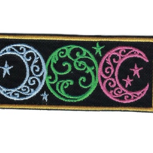 May include: A black embroidered patch with three crescent moons, each with a different color and design. The moons are surrounded by a gold border.