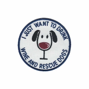 May include: A white round embroidered patch with a blue border. The patch features a cartoon dog with a wine glass in its mouth. The text on the patch reads "I just want to drink wine and rescue dogs".