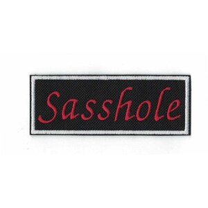 May include: Black and white rectangular patch with a white border. The word "Sasshole" is embroidered in red.