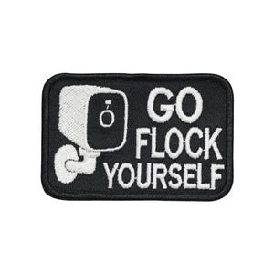 May include: A rectangular embroidered patch with a black background and a white border. The design features a white security camera icon on the left and the white text "GO FLOCK YOURSELF" stacked in three lines on the right side of the patch.