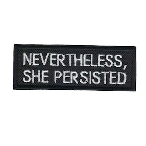 May include: Black embroidered patch with white text that reads "Nevertheless, She Persisted."