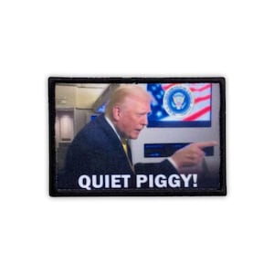 May include: A rectangular patch with a black border. The image inside shows a man in a suit pointing. Behind him is a screen with the American flag and a presidential seal. The text "QUIET PIGGY!" is at the bottom.
