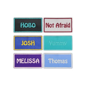 May include: Six embroidered patches with text. The patches are rectangular with various colors and text: "HOBO", "Not Afraid", "JOSH", "Yummy", "MELISSA", and "Thomas". The patches are likely for clothing or accessories.
