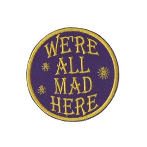 May include: Purple round embroidered patch with gold thread. The patch says "We're All Mad Here" with stars around the text.