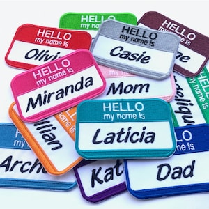 May include: A collection of colorful iron-on name patches with the text "Hello my name is" followed by a name. The names include Olivia, Miranda, Casie, Mom, Laticia, Dad,  Arch, and Kat.
