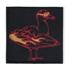 May include: Red and gold embroidered patch of a duck wearing sunglasses and riding a surfboard with flames.