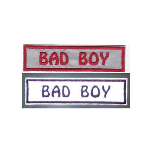 May include: Two embroidered patches with the text "BAD BOY" in red and purple lettering on a white background. The patches are rectangular and have a white border.