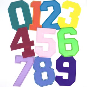 May include: Nine felt patches in different colors, each with a number from 0 to 9. The patches are in a variety of colors, including green, orange, blue, yellow, red, pink, light green, purple, and blue.
