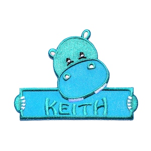 May include: A blue embroidered iron-on patch featuring a cartoon hippopotamus holding a banner with the name "Keith" on it.