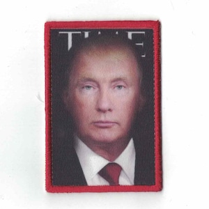 May include: A red framed patch with a black background featuring a photo of a man with blonde hair. The text "TIME" is visible in white at the top of the patch.