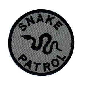 May include: A gray circular patch with black embroidery. The patch says "Snake Patrol" with a snake design in the center.
