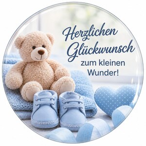 Könnte beinhalten: Ein rundes Dekoschild mit einem hellbraunen Teddybären, der auf einer gefalteten blauen Strickdecke sitzt, neben einem Paar hellblauer Babyschuhe und einem blauen herzförmigen Ornament, mit dem Text Herzlichen Glückwunsch zum kleinen Wunder.