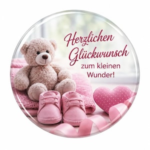 Könnte beinhalten: Ein runder Zierknopf mit einem hellbraunen Teddybären, einem Paar rosa Babyschuhen, einem rosa Herz und einem rosa Band. Der Text lautet Herzlichen Glückwunsch zum kleinen Wunder in dunkelrosa Schreib- und serifenloser Schrift.