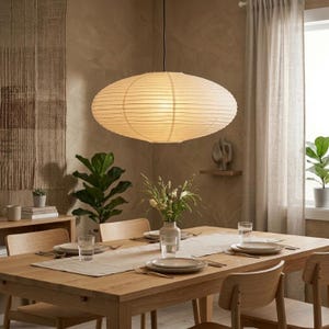 May include: A large, oval-shaped pendant light fixture with a ribbed, off-white paper shade suspended from the ceiling. The lamp features a horizontal, layered texture and emits a soft, warm glow, hanging centered above a wooden dining table.