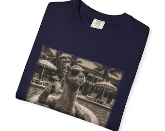 May include: A navy blue t-shirt featuring a sepia-toned graphic print of a camel wearing sunglasses, floating in a swimming pool on an inflatable ring while holding a tropical drink with a small umbrella, set against a resort background.
