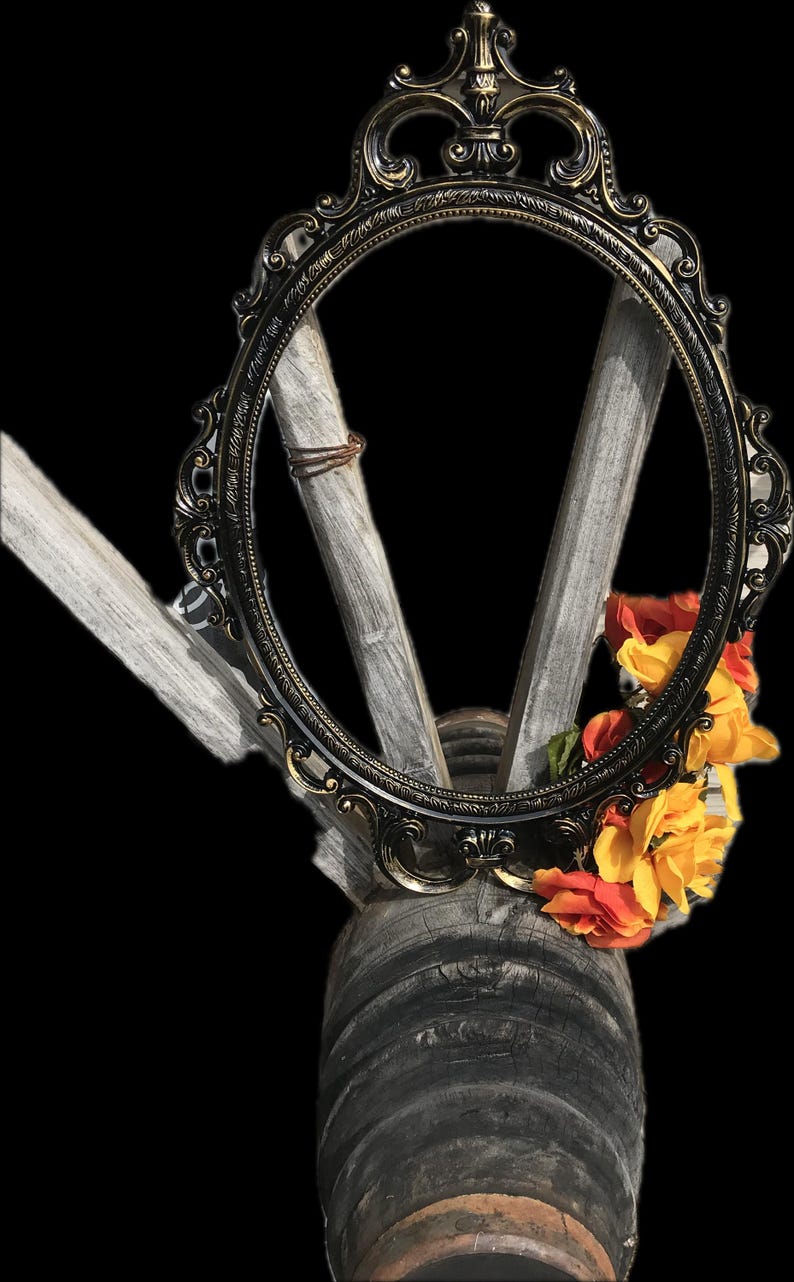 Puede incluir: Marco ovalado ornamentado en negro y dorado con detalles decorativos. El marco se encuentra sobre un fondo de madera envejecida y adornado con flores naranjas y amarillas. El dise&ntilde;o sugiere un tema vintage o r&uacute;stico.