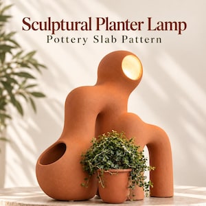 May include: A terracotta-colored sculptural planter lamp with a pottery slab pattern. The lamp features an organic, curved form with a circular light opening at the top and a hollow section for a small potted plant with green foliage.