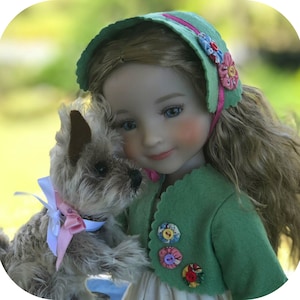 Peut inclure: Une poupée en porcelaine aux longs cheveux bruns porte une veste verte avec des boutons colorés et un bonnet rose et vert. Elle tient un petit chien en peluche gris et brun avec un nœud rose.