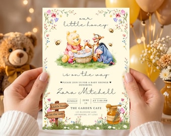 May include: A rectangular baby shower invitation card featuring Winnie the Pooh, Piglet, Tigger, and Eeyore surrounding a baby in a basket. The text reads our little honey is on the way, Zara Mitchell, Sunday June 15 at 3:00 PM, and The Garden Cafe.